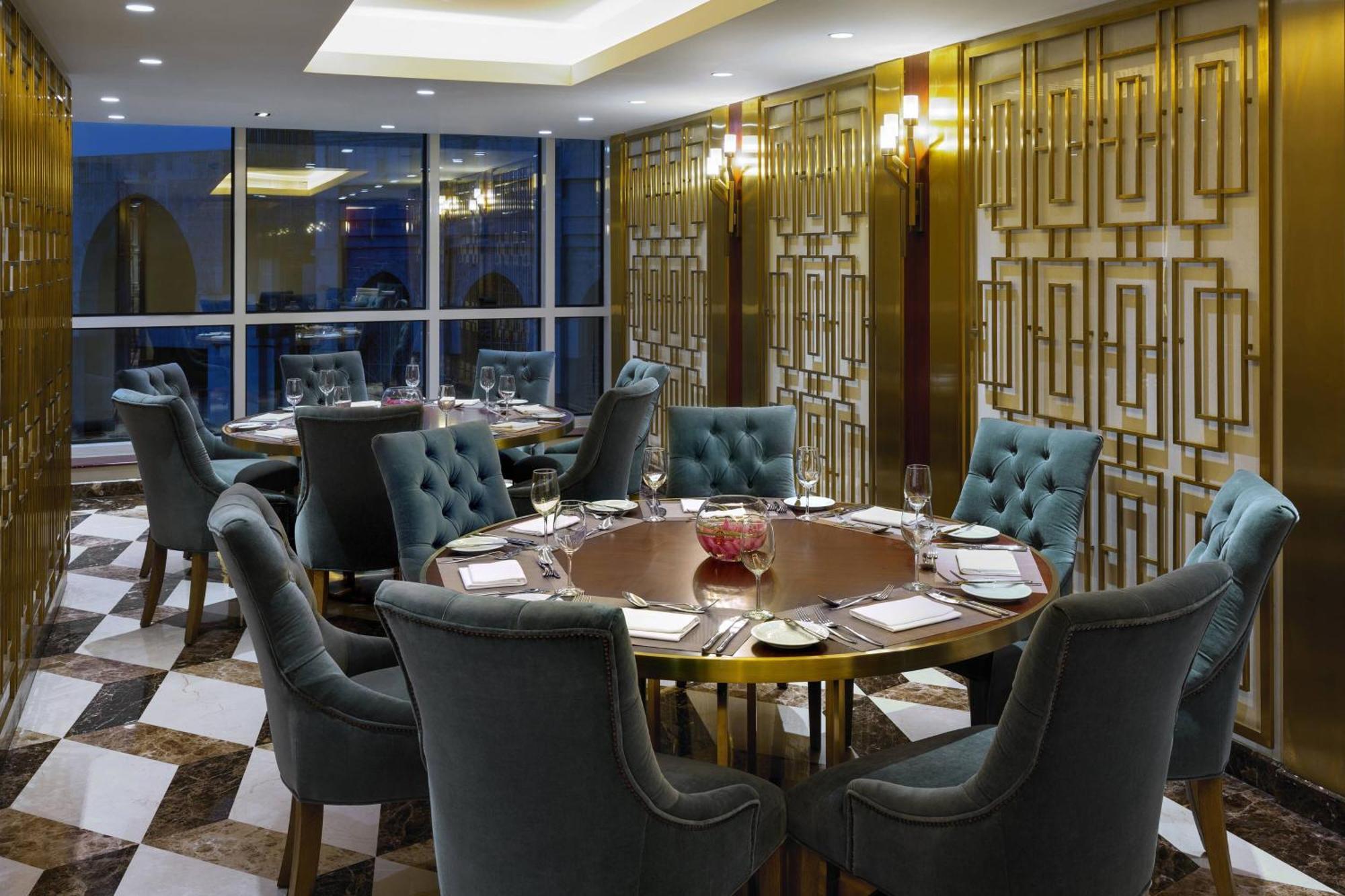 쉐라톤 마카 자발 알 카바 호텔 메카 외부 사진 The photo shows an elegant dining room with a sophisticated ambiance. It features a round wooden table at the center, surrounded by plush chairs upholstered in a soft, teal fabric. The room has a stylish décor, highlighted by a geometrically patterne