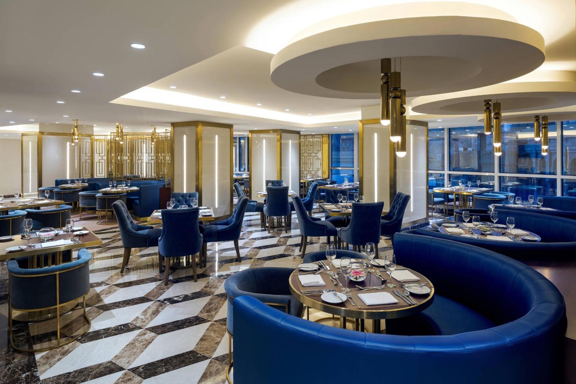 쉐라톤 마카 자발 알 카바 호텔 메카 외부 사진 The photo shows the interior of a modern restaurant. The design features elegant curved blue seating arranged around round tables with plates and glassware set for dining. The flooring is a striking marble pattern, adding to the upscale ambiance. The